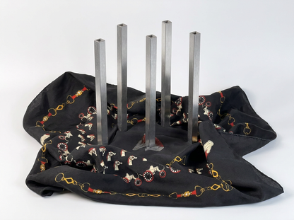 A black fabric cover with a printed pattern of white horses, red accents, and gold horsebit links, draped over a set of five silver metal pedestal legs on a white studio background.
