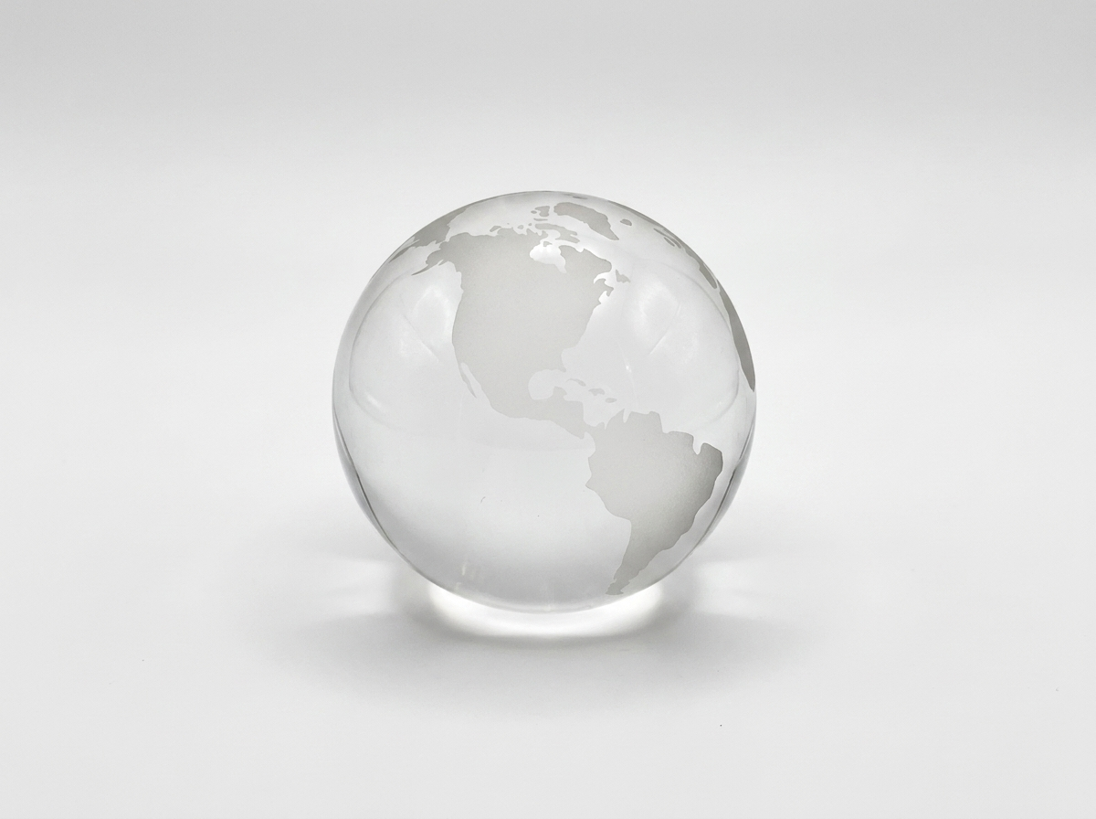 A clear glass globe desk ornament with a frosted etched map design, on a light gray background.