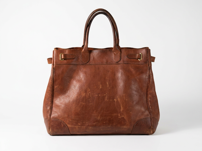 A brown leather tote bag with distressed texture, dual top handles, and brass-tone hardware, photographed against a clean white studio background.