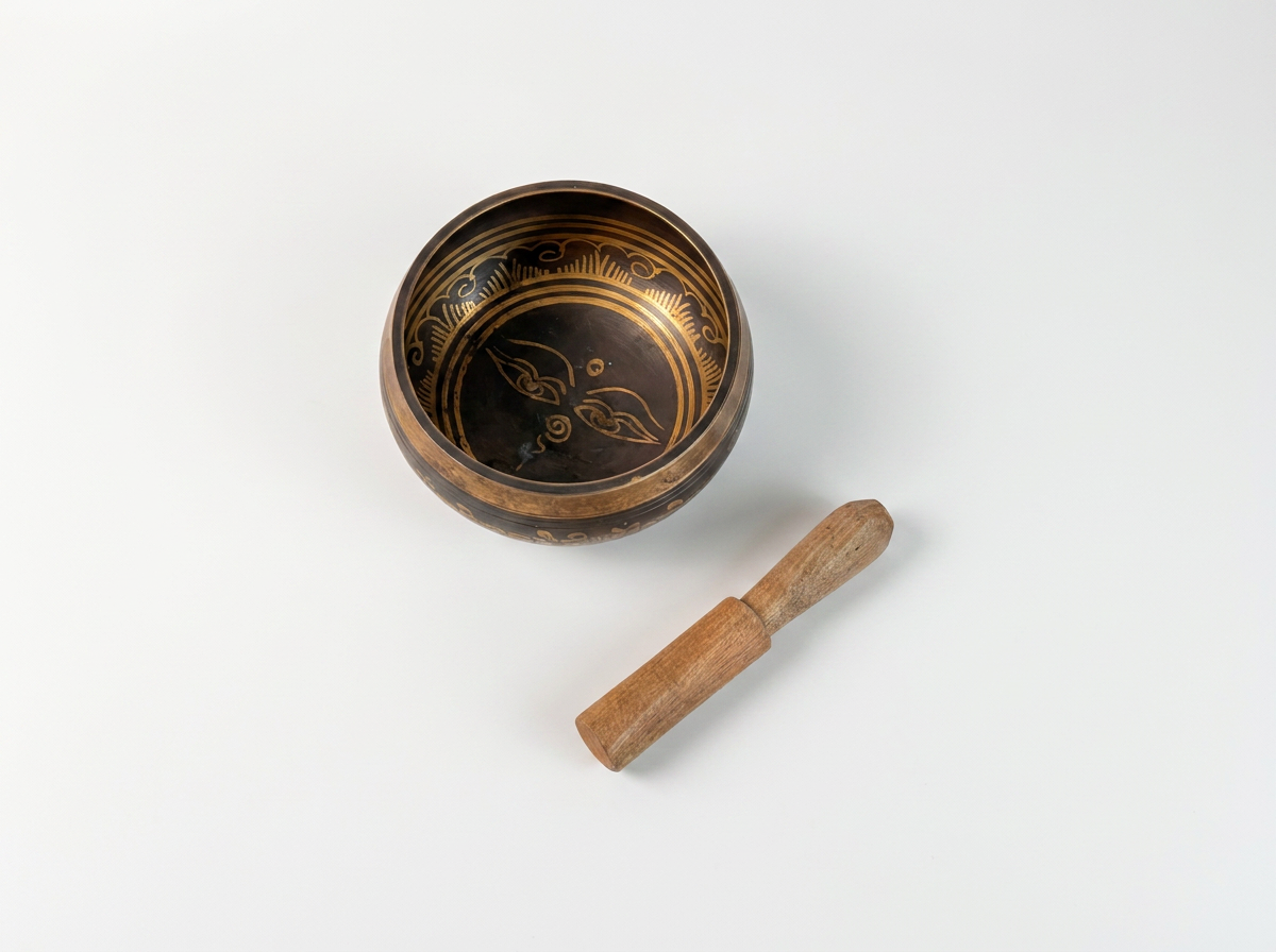 A small round singing bowl with a dark metallic interior and gold decorative markings, shown with a wooden mallet on a plain white background.